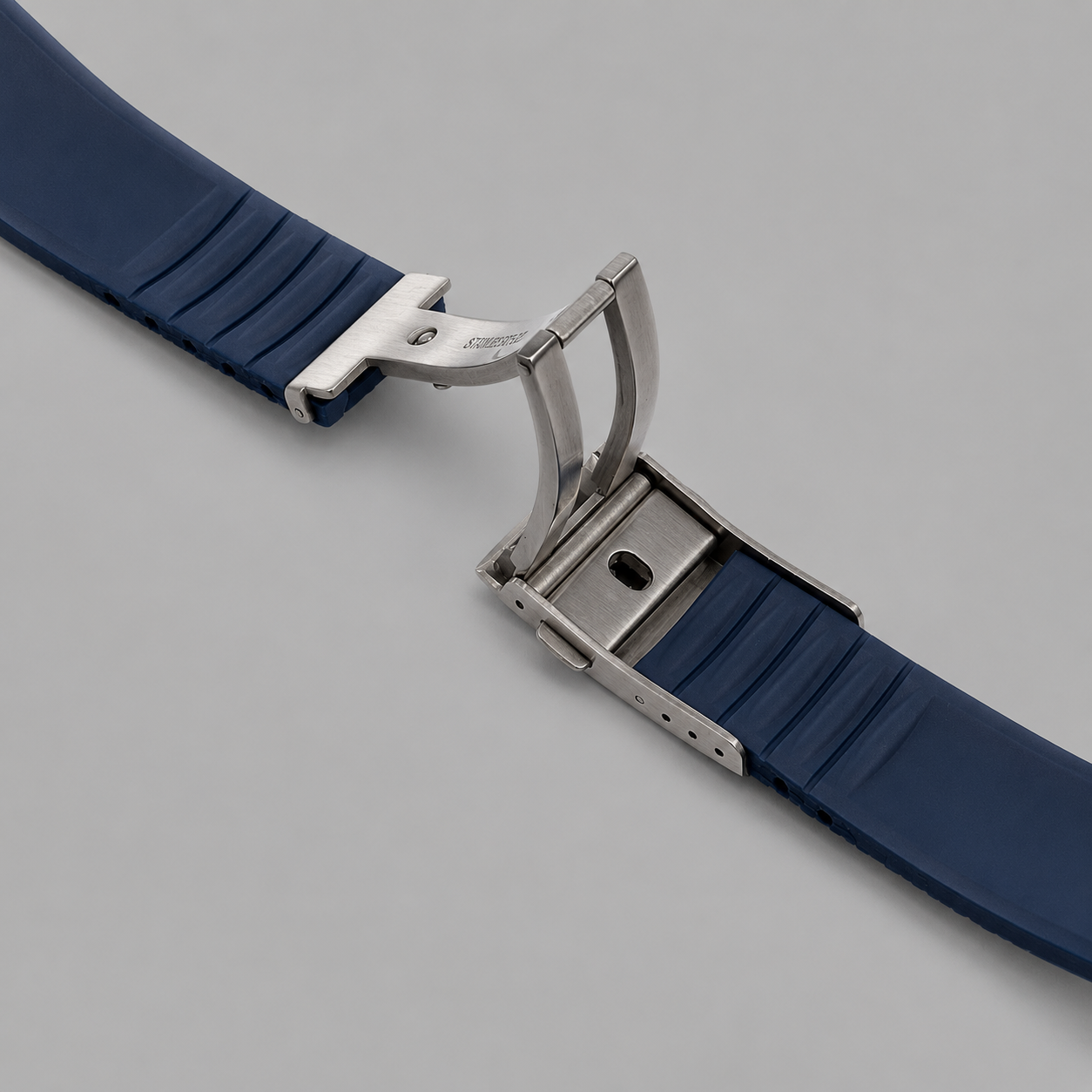 Navy blue FKM rubber watch strap with stainless steel deployant clasp on a light grey studio background.