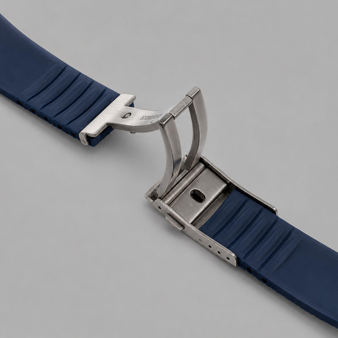 Navy blue FKM rubber watch strap with stainless steel deployant clasp on a light grey studio background.